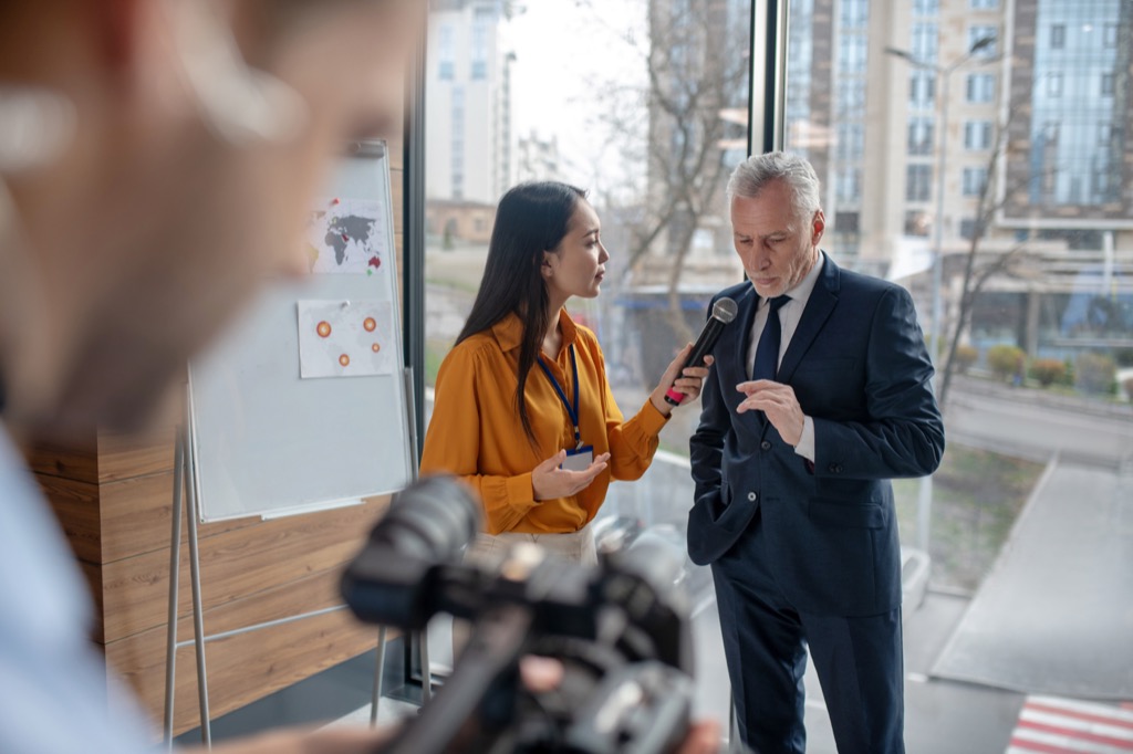 Professionals. Young female reporter looking busy holding a microphone during interview